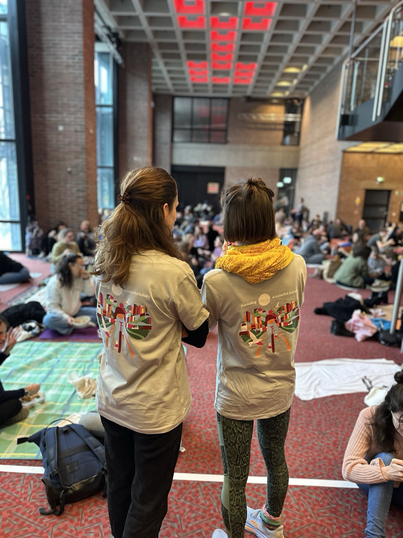 Zwei Gäste in Event-Shirts, Blick in die volle Halle