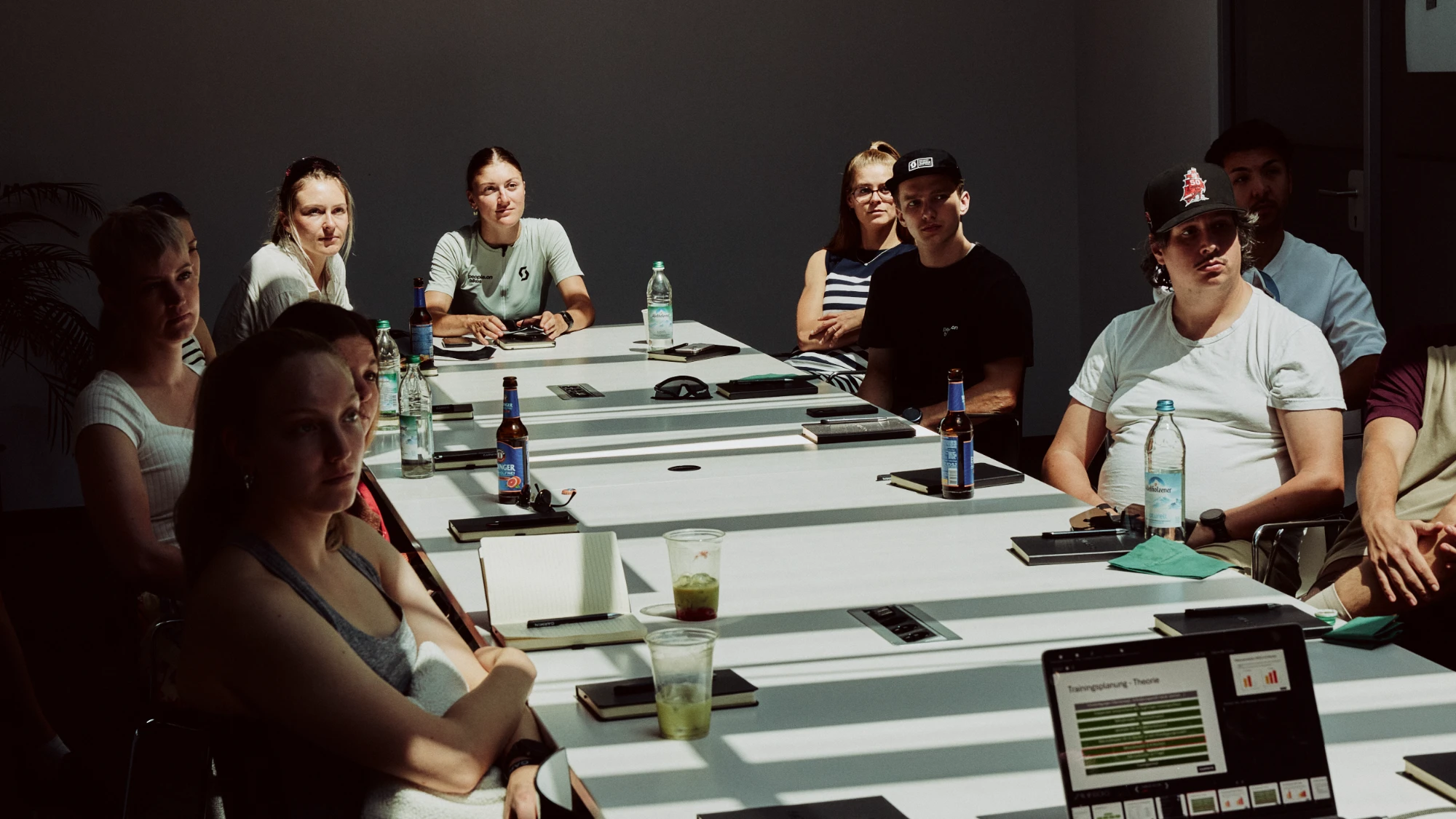 Gruppe am langen Tisch bei einer Arbeitssession, Notizbücher und Getränke auf dem Tisch